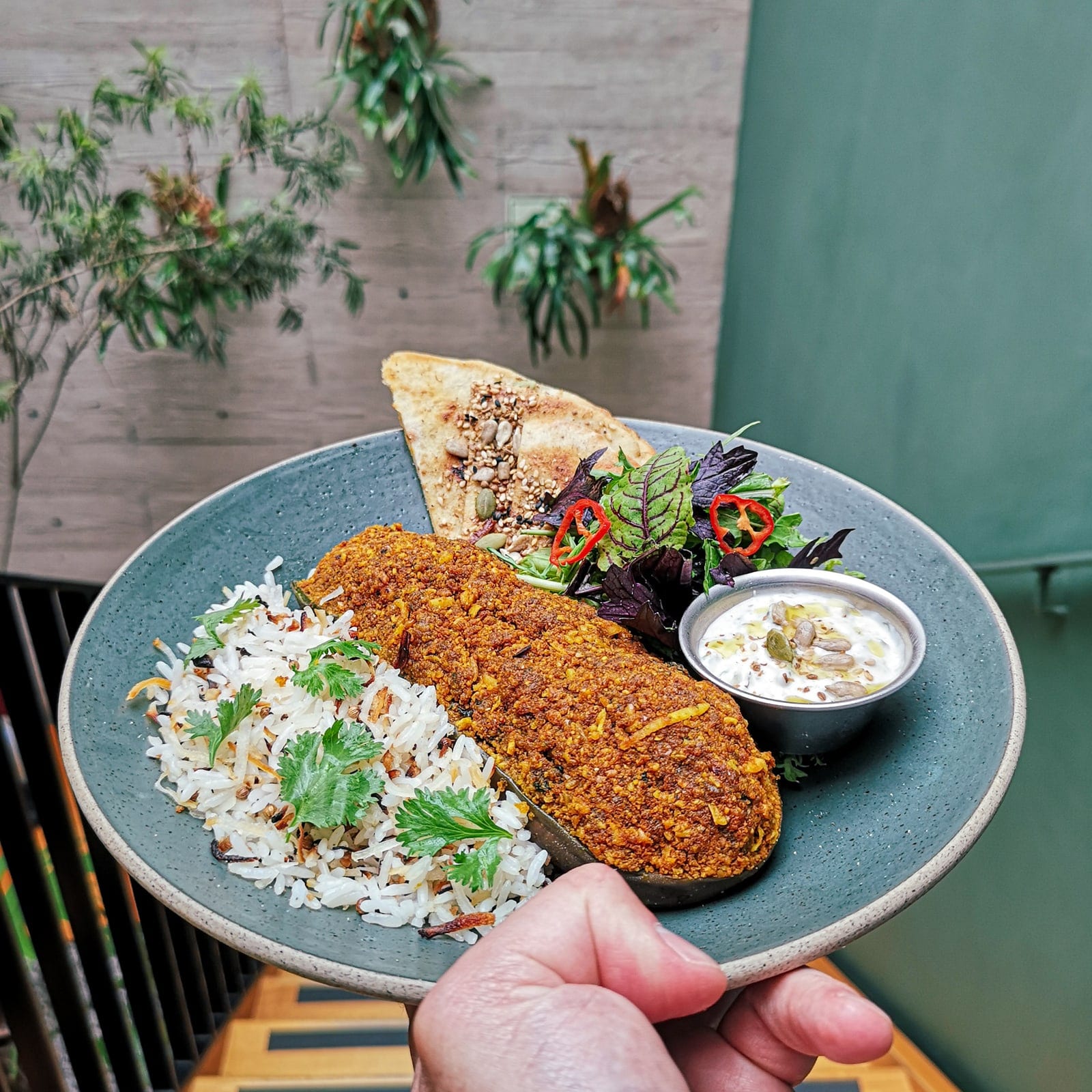 Plato con arroz, verduras y ensalada sostenido frente a la terraza de mó