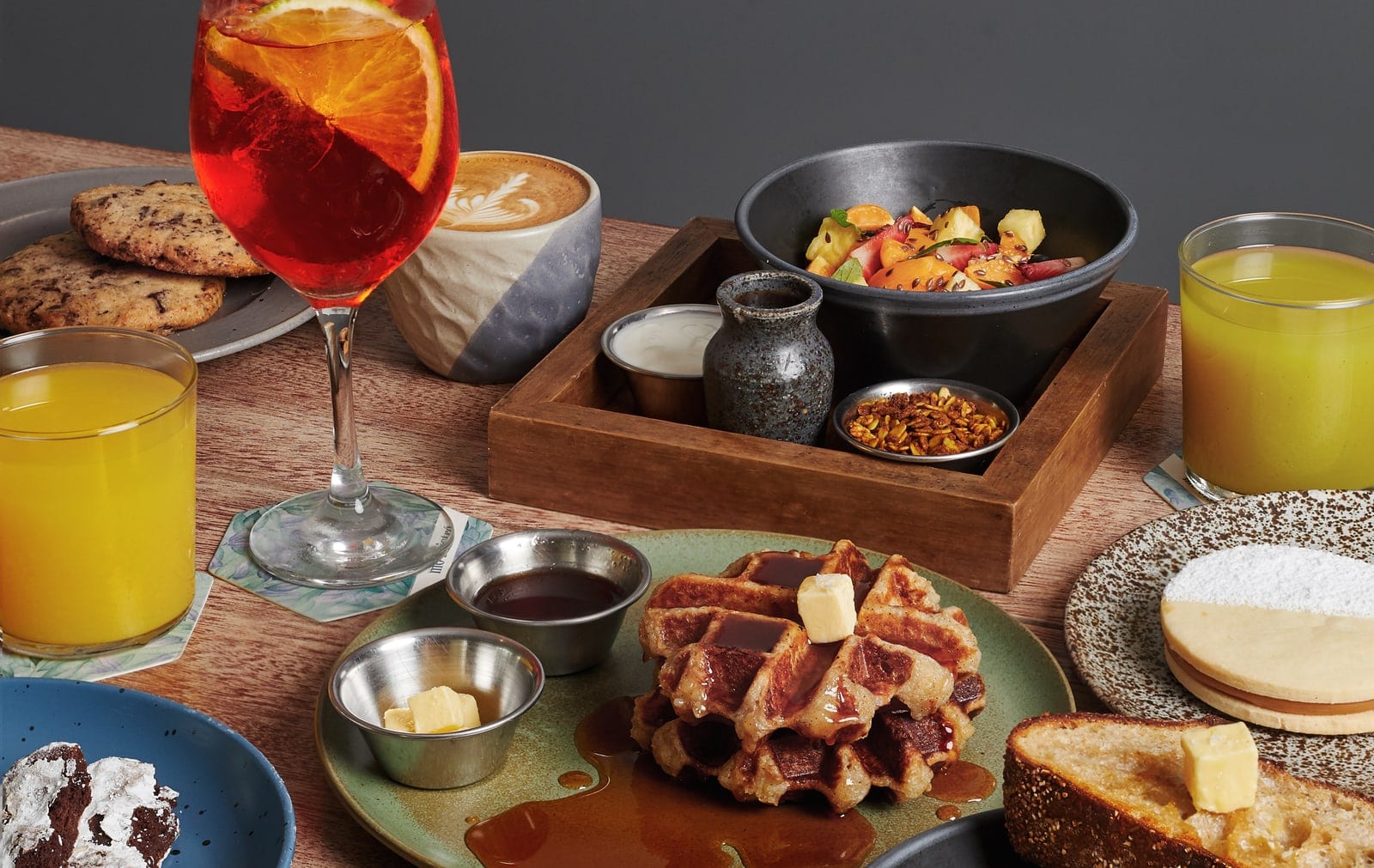 Mesa de mó servida con waffles, sándwich, jugos, café y pastelería